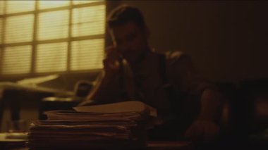 Sepia, cep telefonuyla konuşan sakallı bir adamla masaya uzanmış, arka plandaki loş ışıklı odada koltukta oturan mektup yığınını yakından çekiyor.