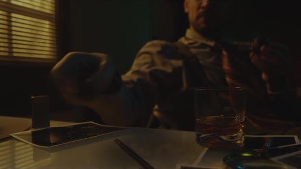在黑暗的房间里看着照片时 一个人坐在桌旁 手里拿着酒杯 点燃着烟斗 带着怀旧之情 拍了一张无法辨认的大胡子男子的中期照片 — 图库视频影像