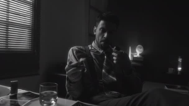 身着复古服装的白胡子男子坐在桌旁 一边为自己的生活后悔 一边抽烟斗 一边看照片和在屋里喝酒 这些画面都是中等的单色镜头 — 图库视频影像