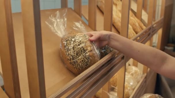 販売のためのディスプレイ棚にゴマの種子と新鮮な焼きパンを配置する女性のパン屋の手の近くのビュー — ストック動画