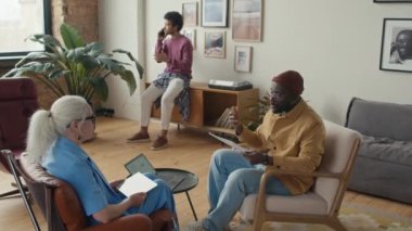 Üst düzey beyaz kadın ve genç siyahi adamın iş projelerini tartışırken, meslektaşlarının iş günlerinde modern rahat ofisinde telefon görüşmelerini aşağı eğ.