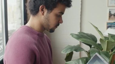 Genç bilişim uzmanının ofis penceresinin önünde durup dizüstü bilgisayarda yazarken çekilen görüntüleri.