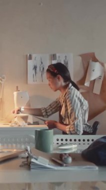 Dikey olarak, terzinin sanayi giyim makinesi ve dikiş fabrikasından geçen kadın çalışanın terzilik kumaşlarını ya da tekstil ürünlerini dikey çekimleri.