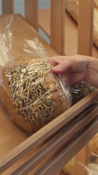 ディスプレイ棚にゴマの種子とパンを置く女性のベーカリーワーカーの垂直クローズアップショット — ストック動画