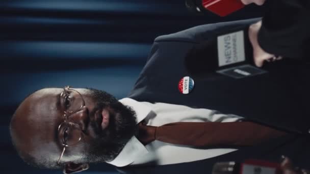 非洲裔美国男性政治家或总统候选人身着西装 打着领带 戴着眼镜 佩戴着选举徽章和美国国旗徽章 在竞选期间在记者面前发表讲话 — 图库视频影像