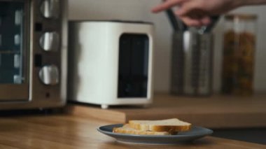 Orta kısımdaki tanınmayan adamın tost makinesinden iki dilim beyaz ekmek alıp tabağa koyduğu ve sonra da modern mutfağa geçtiği fotoğraf.