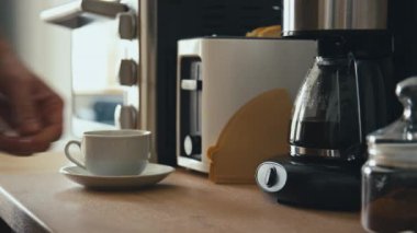 Yandan bıçaklanan erkek elinin kahve makinesi çaydanlığını alıp modern mutfakta beyaz porselen bardağa kahve koyarkenki görüntüleri.