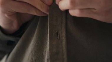 Bıçaklı makro, kapalı alanda giyinirken kapalı kumaştan yapılmış kahverengi gömleğin düğmelerini ilikleyen eller.