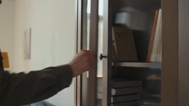 Tanımlanamayan bir adamın, kitaplığı cam kapılı ahşap kitaplığa geri koyması ve modern bir daireye taşınması.
