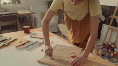 Tulum giymiş, kıvırcık saçlı, eskiz defterinde pastel tebeşirler çizen, mutlu beyaz kadın ressamın orta boy yakın plan portresi. Sonra kameraya bakıp poz veriyor ve gülümsüyor.