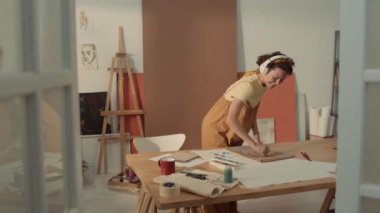 Neşeli, enerjik, kulaklıklı, eskiz defterine soyut resimler çizen, atölyede pastel boya çalan, ilham verici müzikler dinleyen ve sallanan beyaz bir kadın.