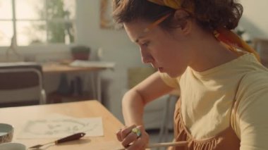 Beyaz bir kadının sanat stüdyosunda masa başında oturup, kil ya da alçıdan yüz heykeli üzerinde çalışırken ve aletler ve ellerle ağız ve burun deliklerini detaylandırırken orta boy yakın çekim.