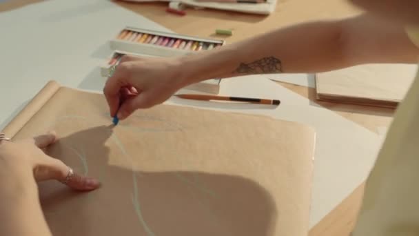 スタジオで働いている間 ベージュペーパーの将来のアートワークのためのスケッチを描いたスタイリッシュなタトゥーと銀のリングを持つ認識できない女性アーティストの手のクローズアップショット — ストック動画