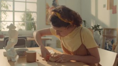 Kafkasyalı kadın ressamın çalışma masasında buharı tüten kahve ve sanat eserleriyle oturduğu ve aletlerle alçı yüz maskesi yontup oyduğu orta boy bir fotoğraf.