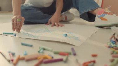 Kotlu kadın ya da kızın, spor salonunda ya da evde yerde oturan spor ayakkabıları ve renkli tebeşir ya da pastel boyalarla kağıda resim çizen tanınmamış kadın ya da kızın yakın çekimleri.