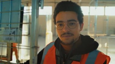 Geniş bir depolama odasındaki mesai saatlerinde depoda çalışan ve elinde stok arabasıyla poz veren Melez bir erkek çalışanın yavaş yavaş portresi.