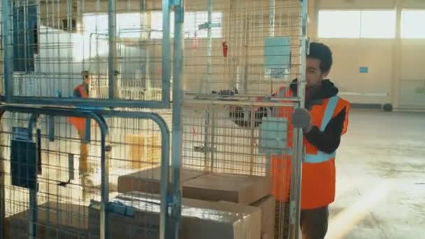 男性のBiracial倉庫労働者の追跡ショット 広々とした貯蔵室の仕事の間に商品を運ぶ箱が付いている貯蔵カートを引っ張ります — ストック動画