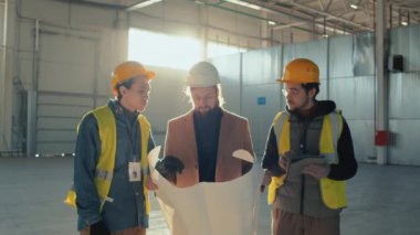 Kafkasyalı işadamı ve iki inşaat mühendisinin bina planı uygulaması üzerinde pazarlık yaparken, planlara ve işçilerin boş binalardaki tabletlere notlar alırken orta büyüklükte bir fotoğrafı.