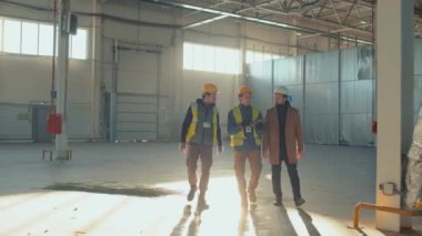 İki inşaat mühendisinin, boş bir bina boyunca yürürken tableti işaret eden iş adamına bina planının uygulanmasını açıklayan uzun metrajlı izleme görüntüleri.