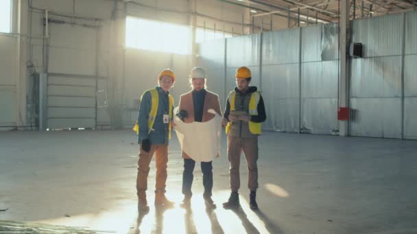 广博的白种人商人身穿休闲装 拿着建筑图则 与位于新宽敞建筑中心的两名伯利兹男性建筑工人讨论其实施情况 — 图库视频影像