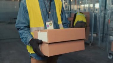 İç mekanlarda nakliye için karton kutular taşıyan tanınmayan bir depo çalışanının orta bölüm izleme görüntüsü.