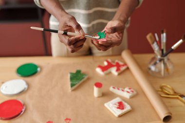 Elinde boya fırçası olan tanınmayan genç bir kadının elleri yeni bir ilk ağaç süsü ya da masa tarafından yazılmış bir Noel sembolü oluşturuyor.