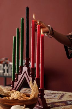 Kwanzaa kutlamalarına hazırlanırken mumları mumlara tutuşturan tanınmamış Afrikalı Amerikalı genç bir kadının eli.
