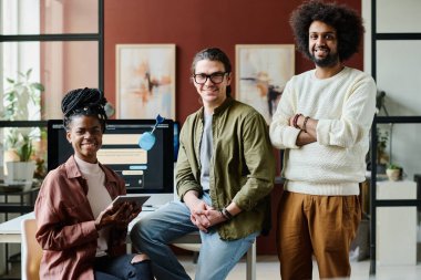 Bir grup başarılı yapay zeka tasarımcısı iş yerinden kameraya bakarken bir tanesi kültürler arası iş arkadaşlarının yanında duruyor.