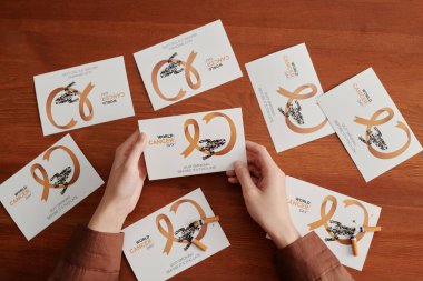 Genç bir kadının kartpostalını ahşap masanın üzerinde tutması ve akciğer kanseri sembolünü ve sigara karşıtı sloganı gösteren diğer kartların olduğu açı.