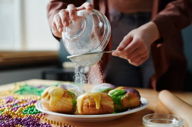 Mardi Gras 'ya hazırlanırken iştah açıcı ev yapımı çöreklerin üzerinde şeker tozu içen tanınmamış genç bir kadının elleri.