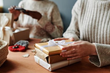 Bir yığın paketlenmiş ve paketlenmiş Noel ya da yeni yıl hediyelerinin üzerinde ipek beyaz kurdeleyle süveter giyen kızların elleri