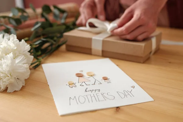 印有母亲节快乐图景的手工明信片放在桌上 旁边放满了白色的康乃馨和打包好的礼品盒 — 图库照片