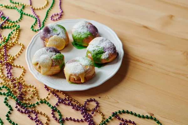 Üzerinde tatlı pudra serpiştirilmiş beş iştah açıcı donut tabağı yeşil, mor ve sarı boncuklarla süslenmiş ahşap masanın üzerinde duruyor.