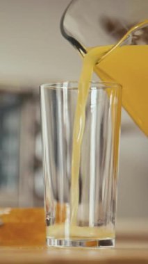 Dikey olarak, bardakları portakal suyuyla doldururken ve mutfaktaki masadan cam alırken.