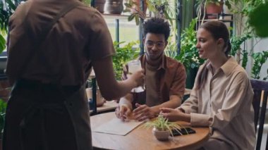 Orta boy gülümseyen beyaz bir kız ve Orta Doğulu bir adam rahat bir restoranda oturmuş sohbet ediyor, heyecanlı bir şekilde siyahi garson onlara içki getiriyor, bırakıyor ve gidiyor.