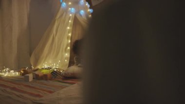 Peri ışıklarıyla süslenmiş oyun çadırında yerde yatan ve modern yatak odasında tabletle oynayan beş yaşındaki Afro-Amerikan bir çocuğun görüntülerini tarıyorum.