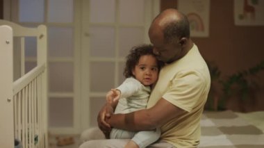 Afrika kökenli Amerikalı bir babanın yatakta oturup kucağında iki yüzlü bir bebekle konuştuğu ve geceleri yatak odasında uyumasını söylediği orta boy bir fotoğraf.