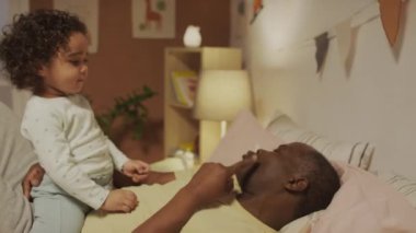 Afrika kökenli Amerikalı bir babanın yatakta yatıp, gece yatak odasında onu dudaklarından ve yanaklarından öpen küçük melez bir kızdan öpücük isterkenki resmi.