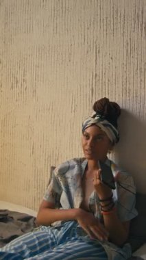 Saç bandı takmış güzel siyahi bir kadının evde oturup hoparlörle sesli mesaj kaydettiği dikey görüntüler.