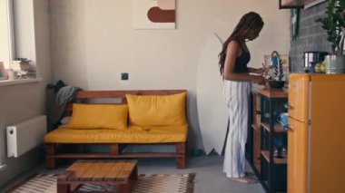 Kanepeye oturmuş mısır gevreği kasesi yiyen ve sabahları Grunge Loft apartmanına bakan Afrikalı genç bir kadının tam boy görüntüleri.