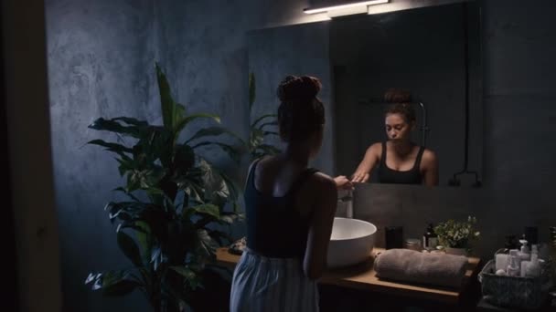 Tylne Ujęcie Młodej Afroamerykanki Myjącej Twarz Wodą Przed Lustrem Ciemnym — Wideo stockowe