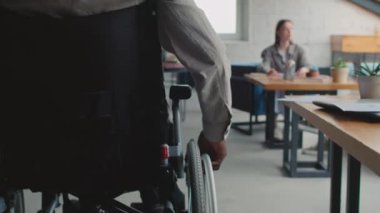 Tekerlekli sandalyedeki siyahi bir adamın ofis binasında dolaşırken, iş arkadaşlarına yaklaşırken, iş teklifinin çıktılarını verirken ve bunu tartışırken yakın plan görüntüsü.