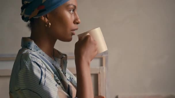 ヘアバンドで若いアフリカ系アメリカ人女性のサイド傾斜クローズアップ お茶や自宅でマグカップからコーヒーを飲んで離れて見る — ストック動画