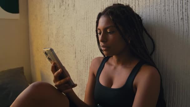 在有霓虹灯标志的阁楼现代公寓里 非洲裔美国年轻女士的侧胸 戴着盒子辫子 一边在电话里抽烟一边抽烟 — 图库视频影像