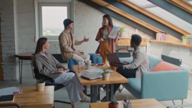 Full zoom shot of diverse startup team having business meeting in loft coworking office - Asian woman presenting graph with growth strategy, others listening, asking questions and arguing