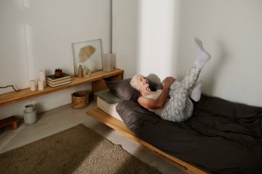 Siyah battaniye ve yastıkla yatakta uzanıp fiziksel egzersiz yaparken uyurgezer bir kadın bacak kaldırıyor.