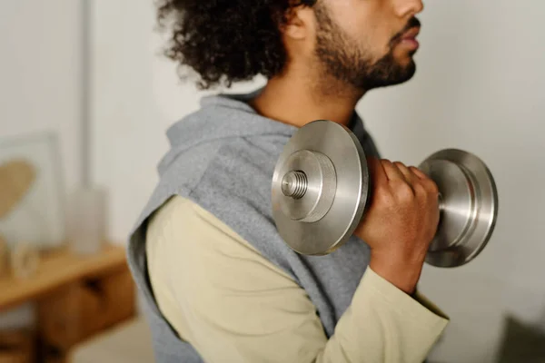 Heavy metallic dumbbell in hand of young active man standing in front of camera during morning physical training and doing exercise