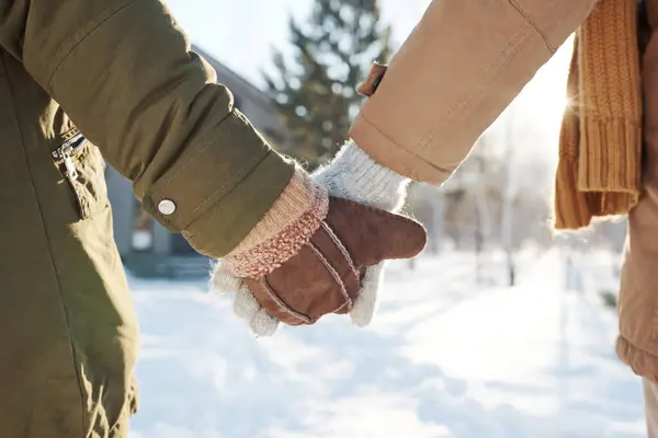 Close-up of hands in mittens and gloves and warm winterwear of affectionate couple standing in front of camera or taking walk