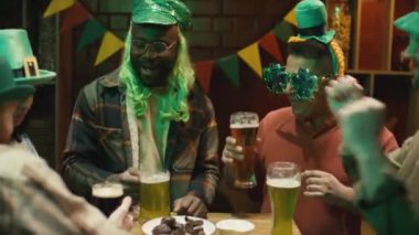 Ulusal İrlanda bayramını yeşil şapkalarla kutlayan ve kulüpte yeşil bira içen çok ırklı erkek ve kadın arkadaş gruplarının orta boy görüntüleri.