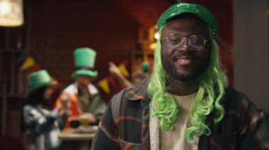 Yeşil peruklu ve parlak şapkalı gülümseyen Afrikalı Amerikalının göğüs portresi. Bardaki İrlanda Ulusal Aziz Patrick Günü partisinde kameraya poz veriyor.